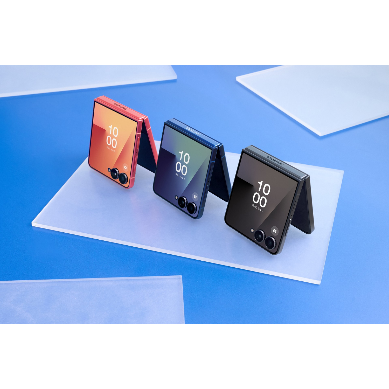 Three foldable phones in orange, blue, and black on translucent plates.