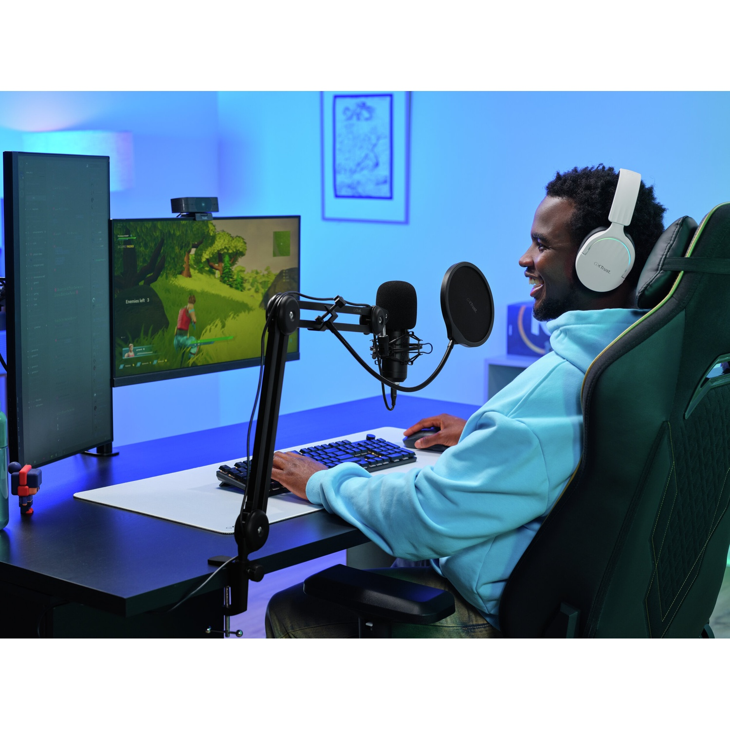 Un uomo in felpa blu gioca ai videogiochi con cuffie bianche.