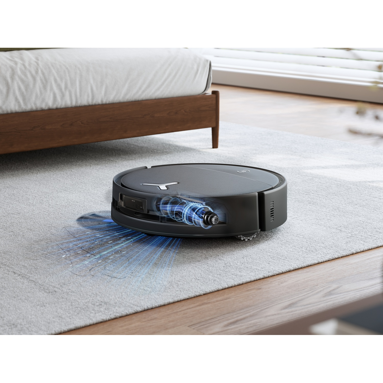 Un robot aspirapolvere nero pulisce un tappeto grigio chiaro vicino a un letto.