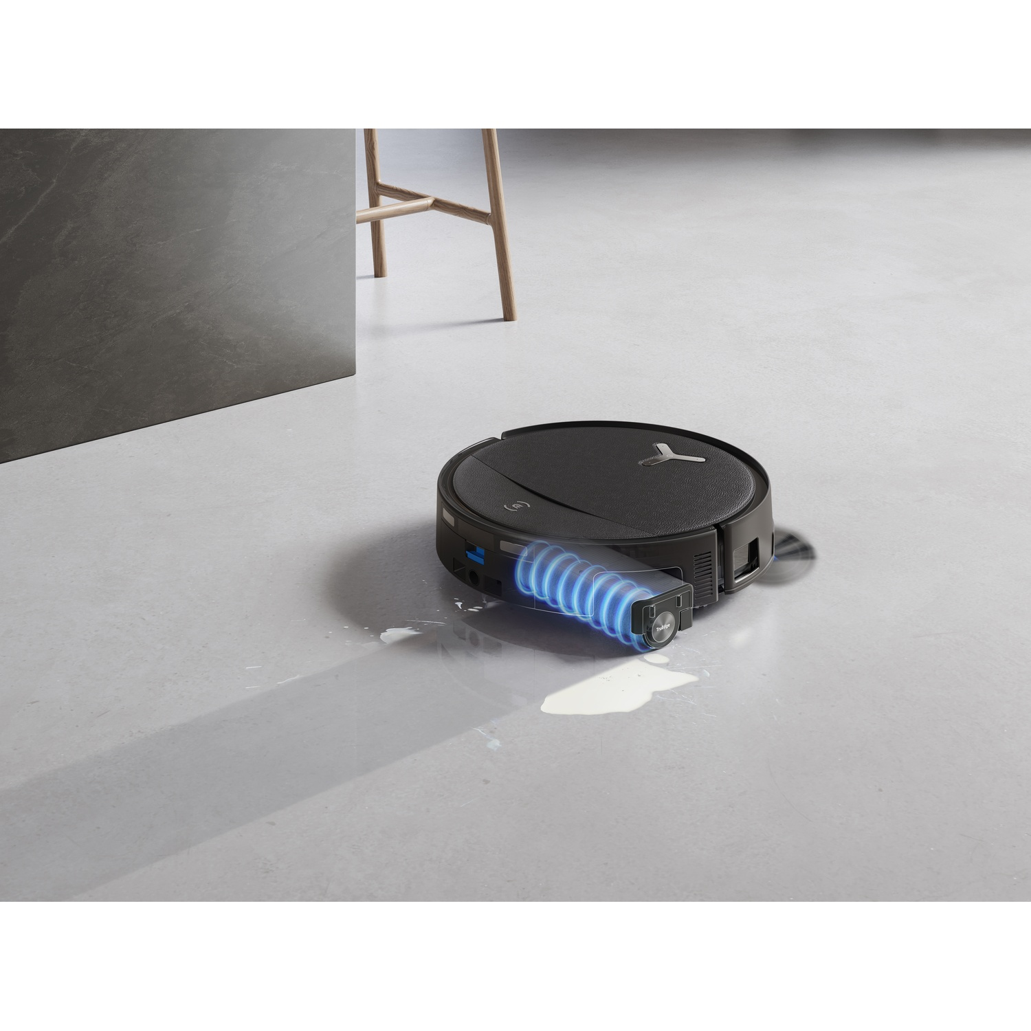 Un robot aspirapolvere nero pulisce macchie d'acqua su un pavimento grigio.