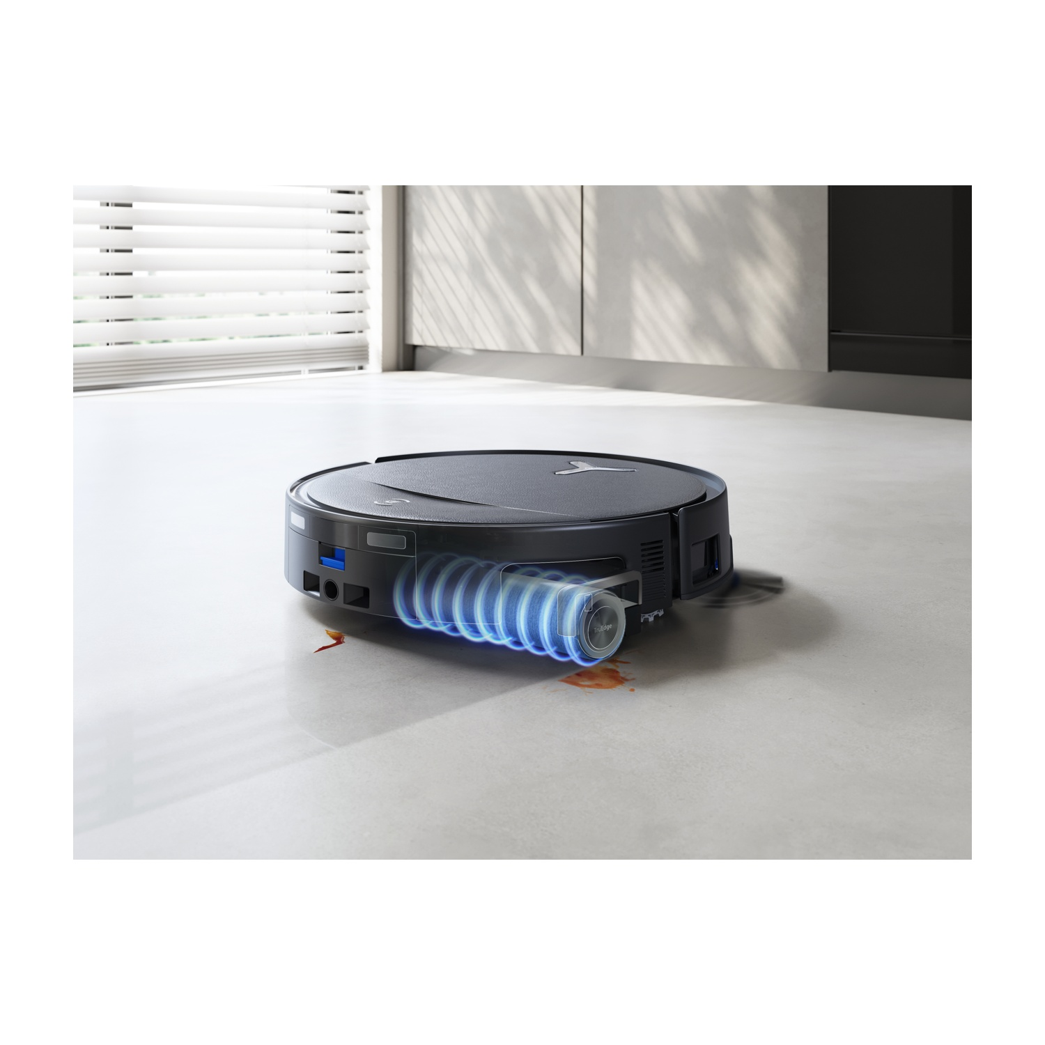 Un robot aspirapolvere nero pulisce una macchia su un pavimento chiaro.