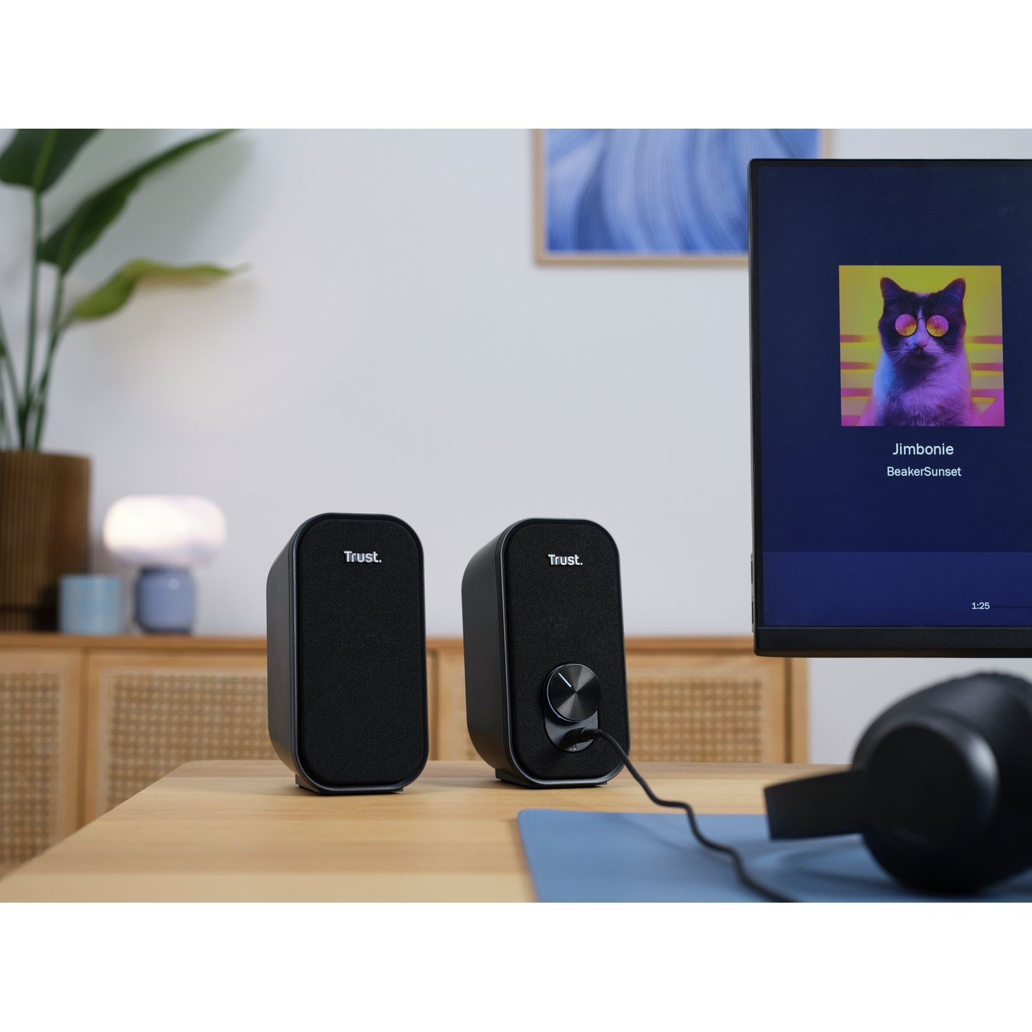 Due altoparlanti neri su una scrivania di legno davanti a un monitor.