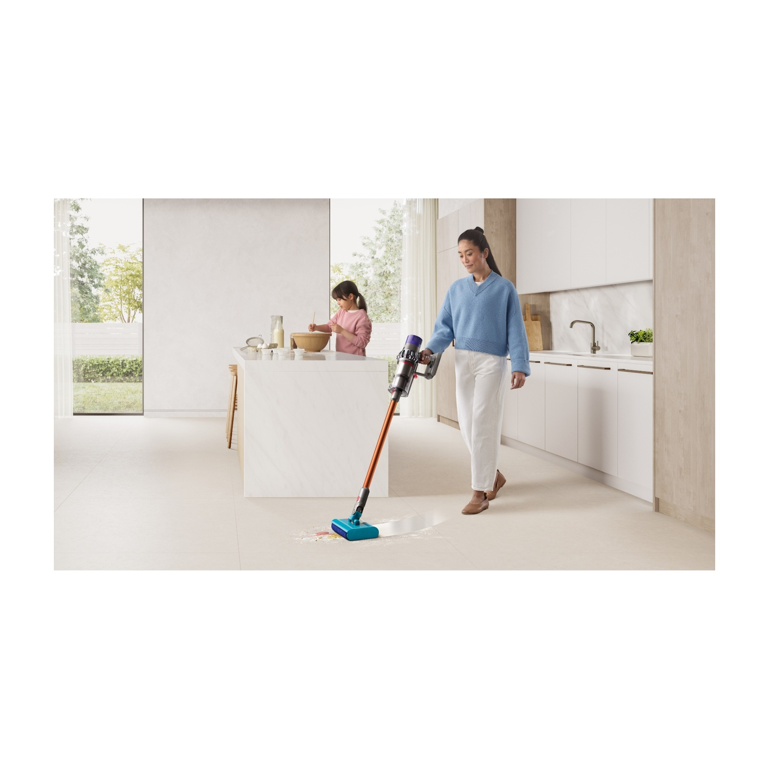 Donna aspira pavimento cucina con aspirapolvere arancio-blu. Bambino cucina.