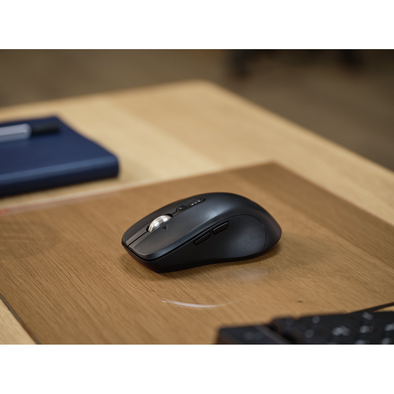 Un mouse per computer nero poggia su una scrivania di legno, accanto a un taccuino blu.
