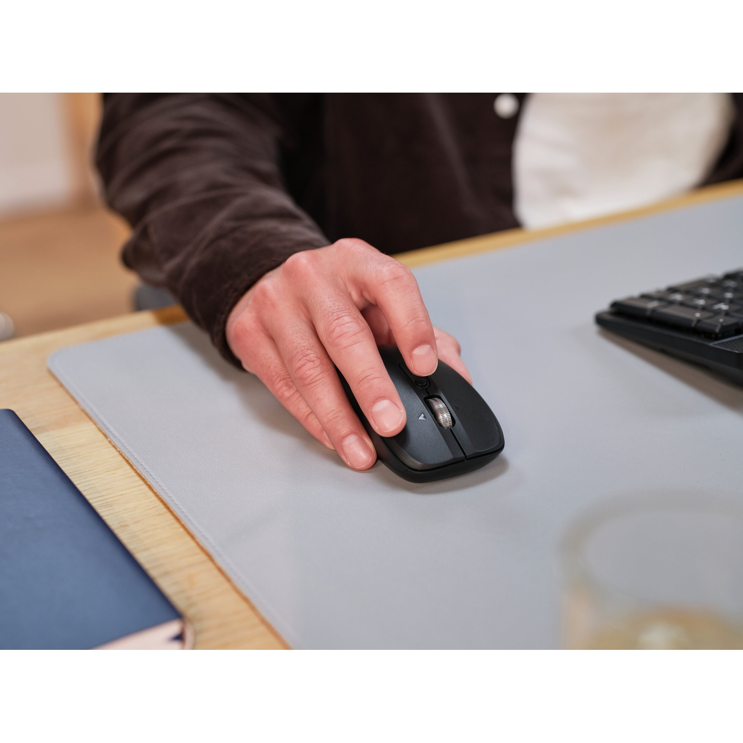 Una mano manovra un mouse nero su un tappetino grigio accanto a un taccuino.