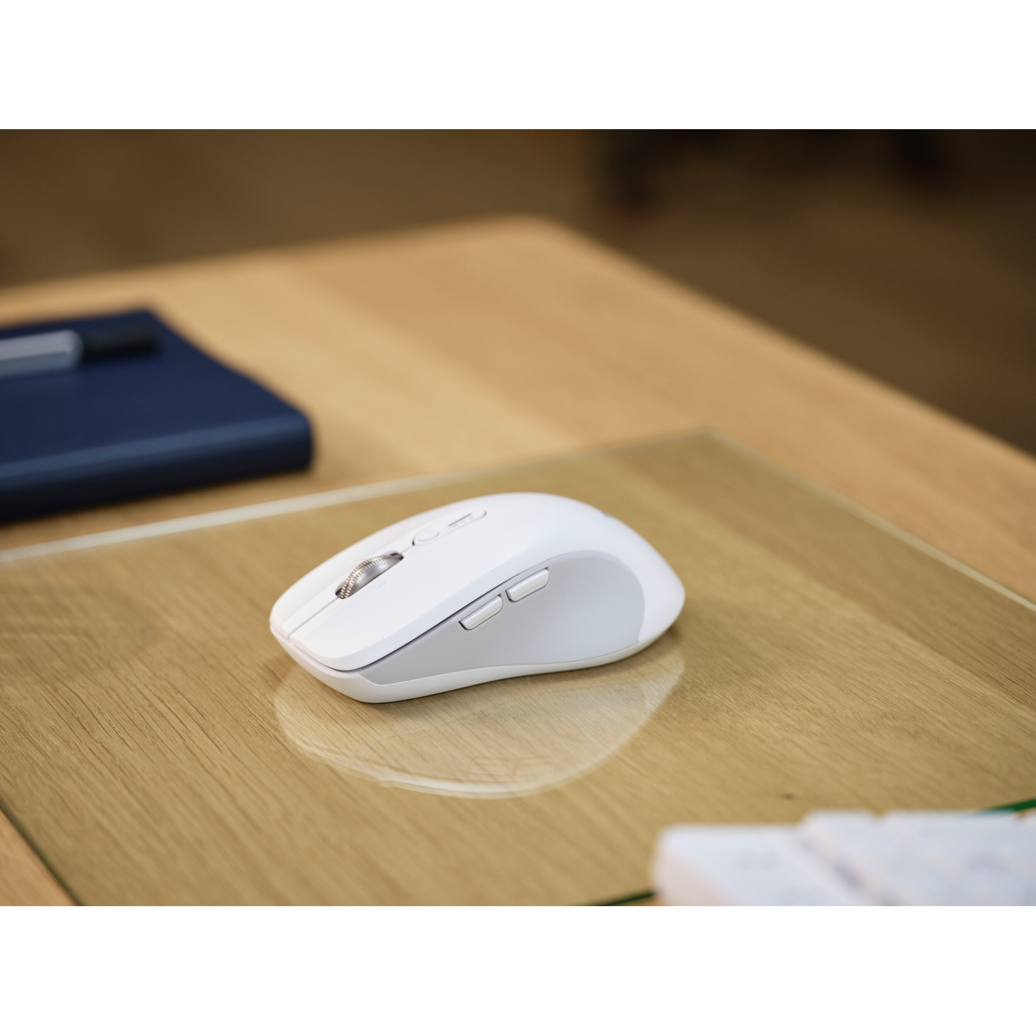Un mouse bianco poggia su una scrivania di legno accanto a un taccuino.