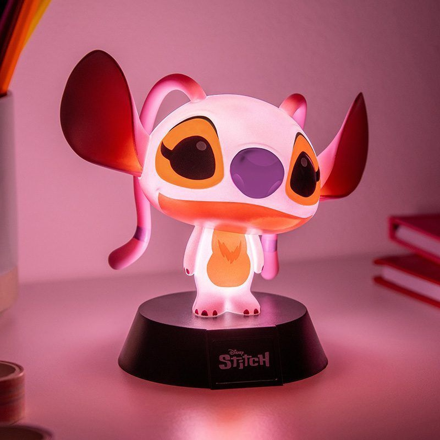 Een gloeiend Stitch figuur staat op een zwarte voet tegen een roze achtergrond.