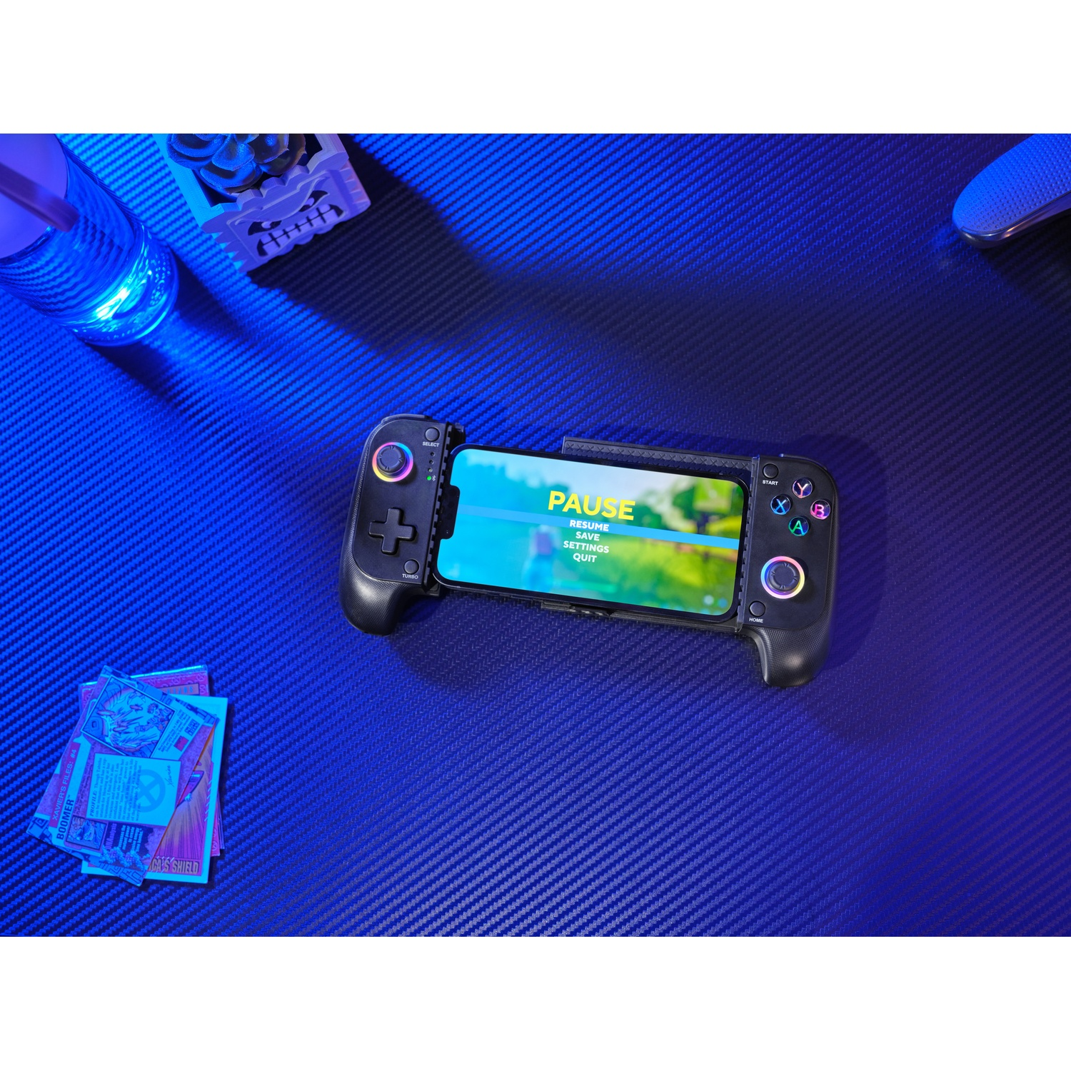 A black game controller holds a phone displaying a pause menu. Cards are on the left.