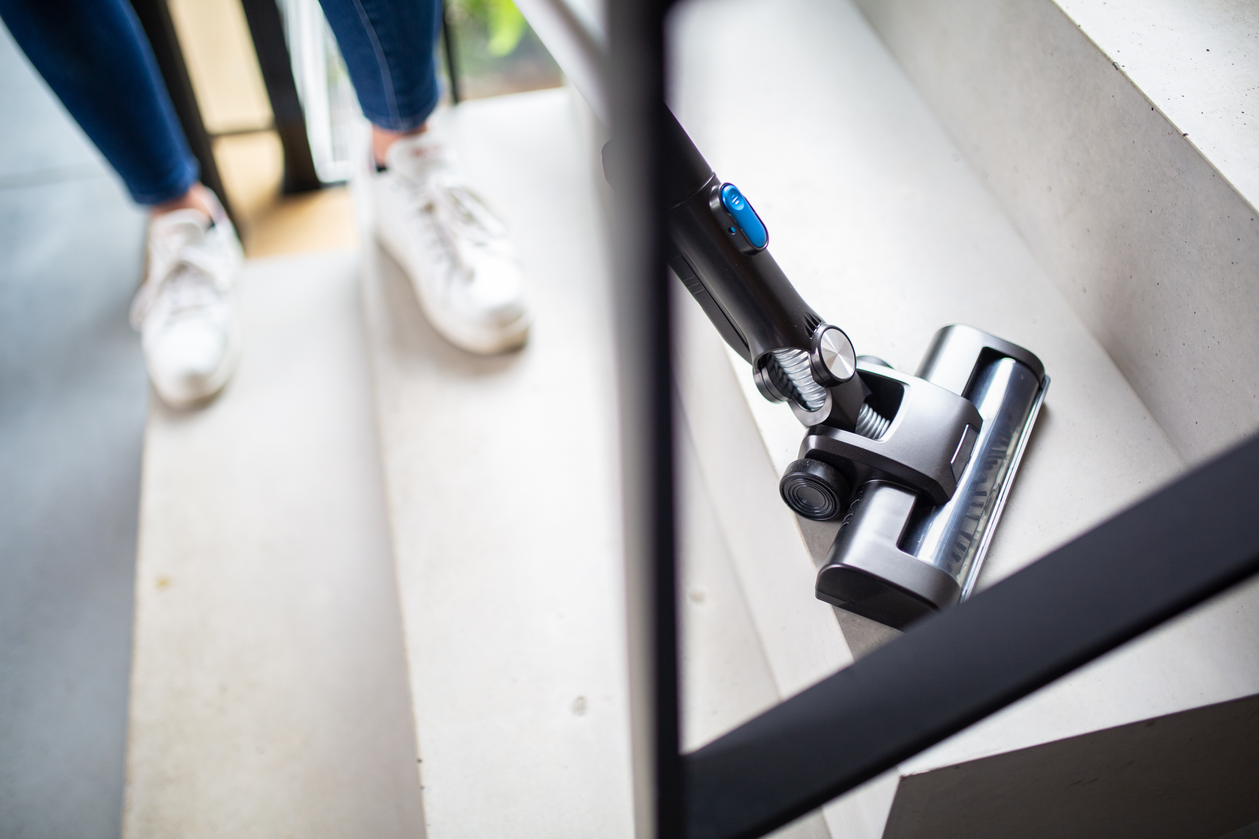 Głowica odkurzacza czyści kamienny stopień, a osoba nosi białe trampki.