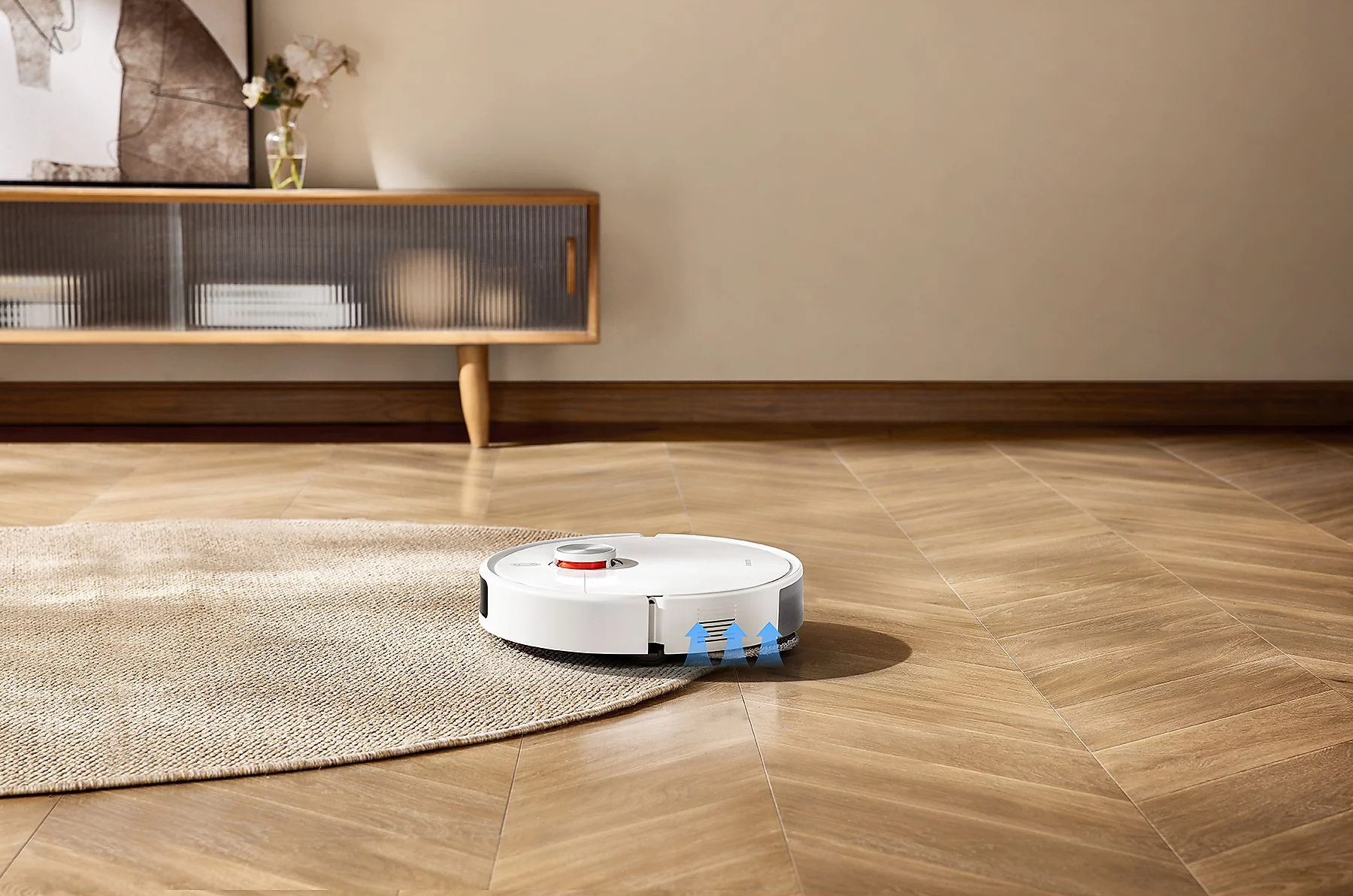 Egy fehér robotporszívó szőnyeg mellett halad el fapadlón.