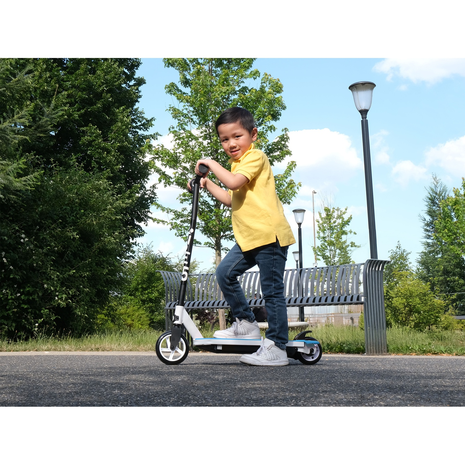 A boy in a yellow shirt rides a scooter in a park setting.