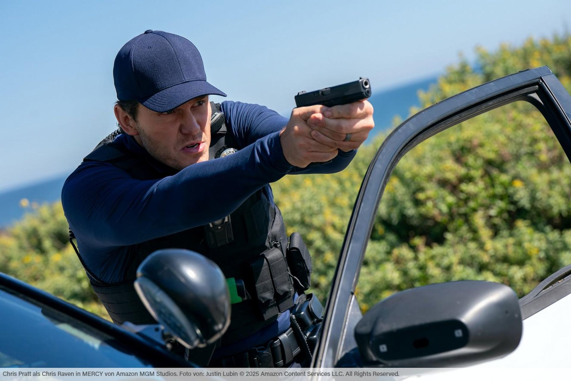 Ein Mann in blauer Uniform und Weste zielt mit einer Pistole aus einem Auto heraus.