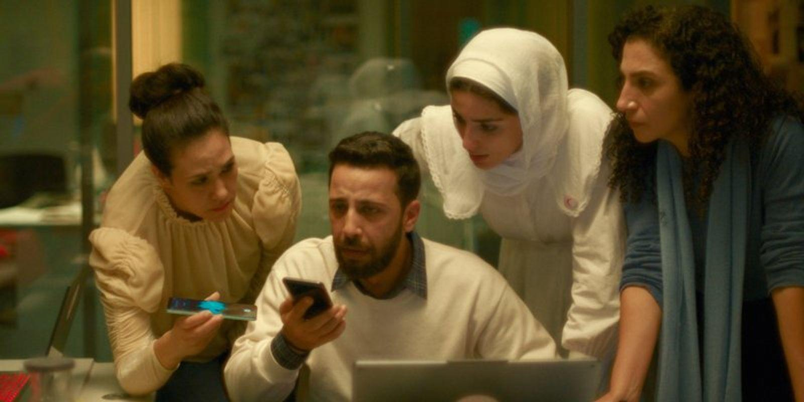 Vier Personen blicken auf ein Smartphone und einen Laptop in einem Büro.
