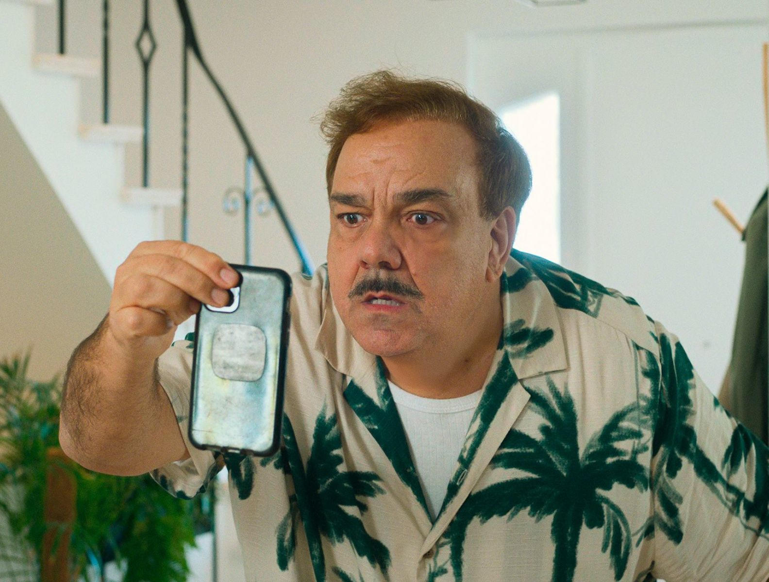 Mann mit Schnurrbart in Palmenhemd hält sein Handy.