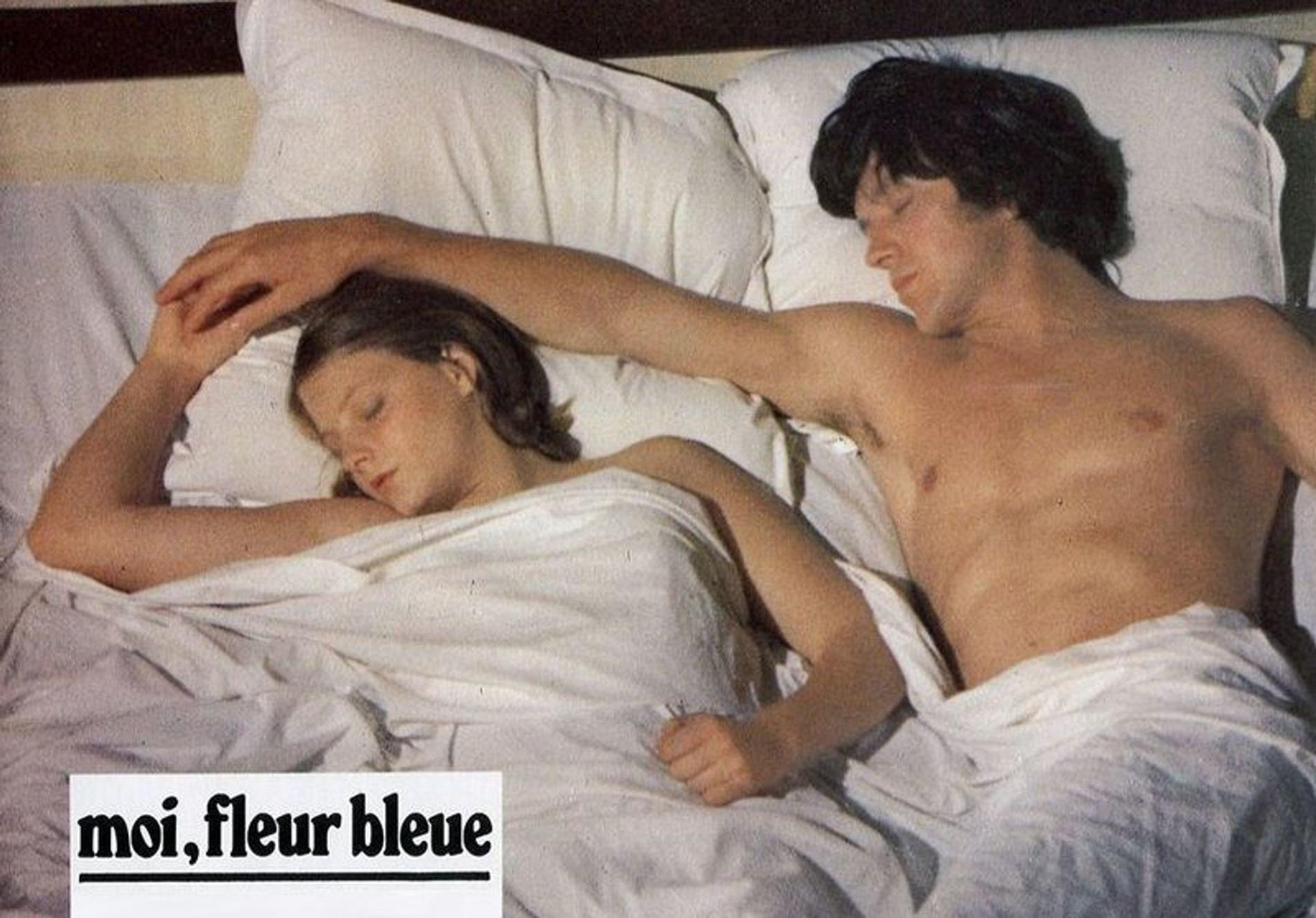 Ein Mann und eine Frau liegen im Bett, bedeckt mit einer weißen Decke.