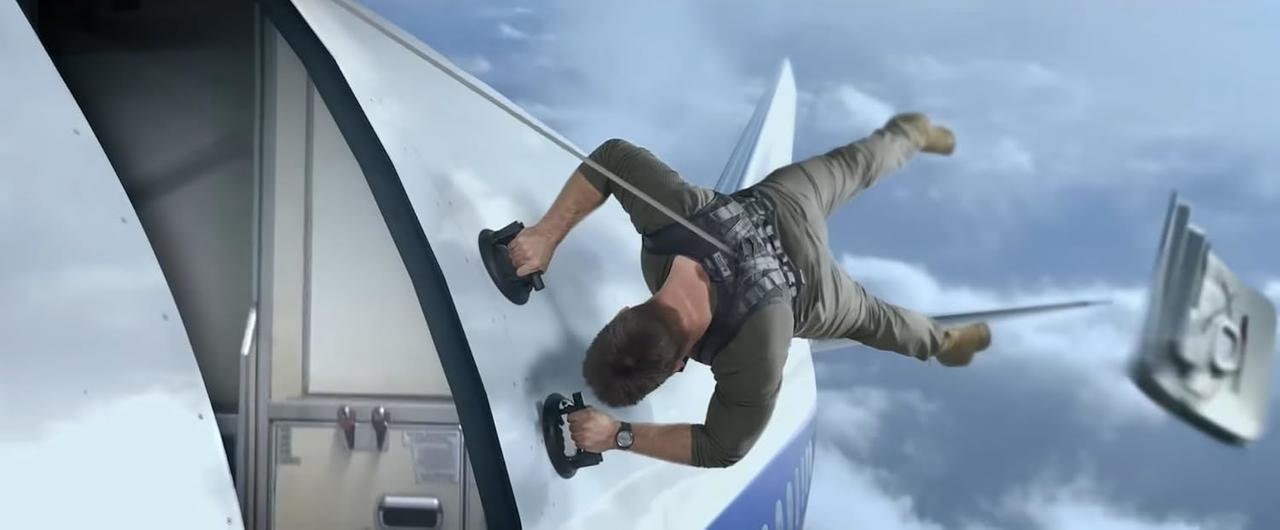 Ein Mann klammert sich mit Saugnäpfen an ein Flugzeug, das in der Luft fliegt.