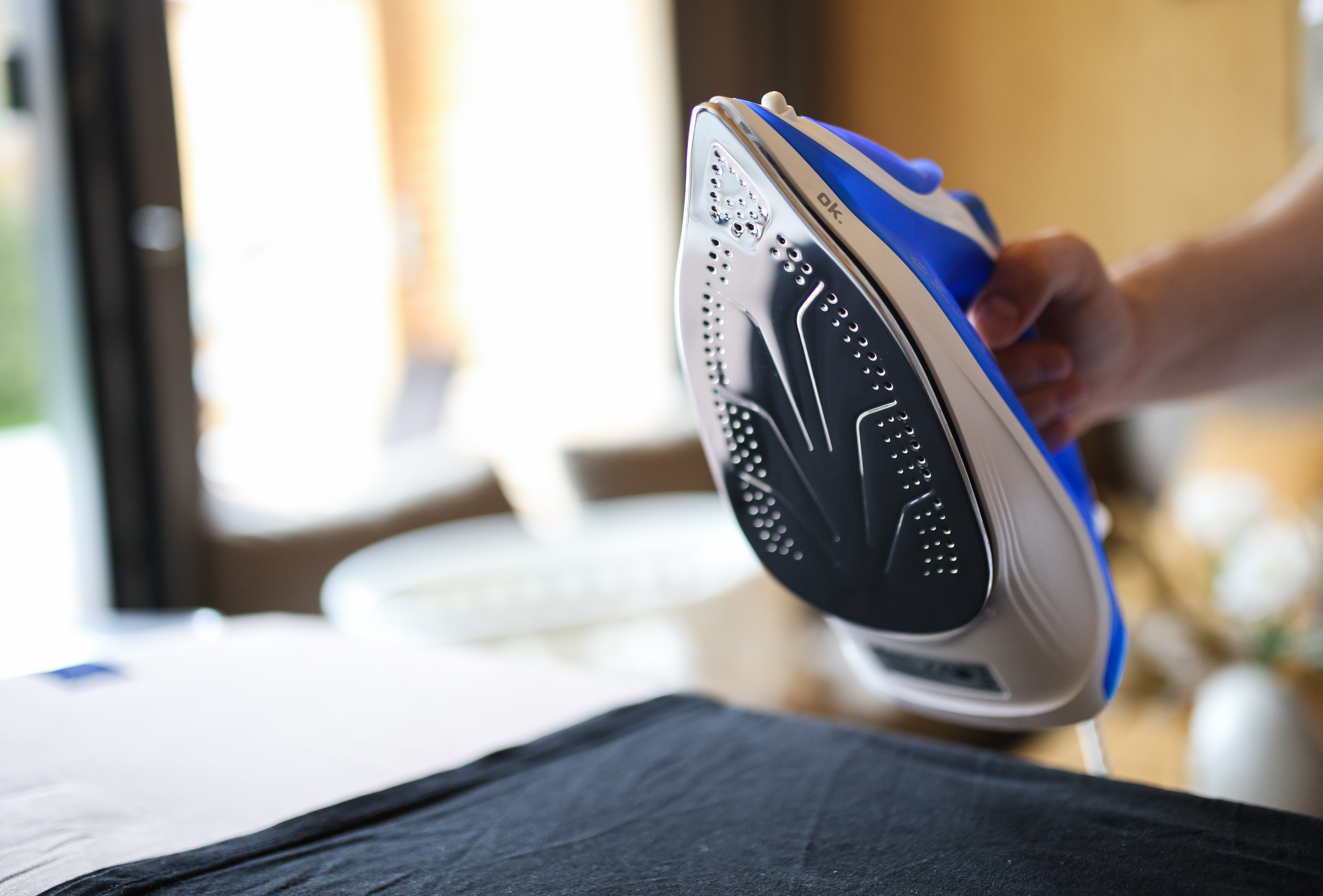 Ręka trzyma niebiesko-białe żelazko nad czarnym i białym materiałem.