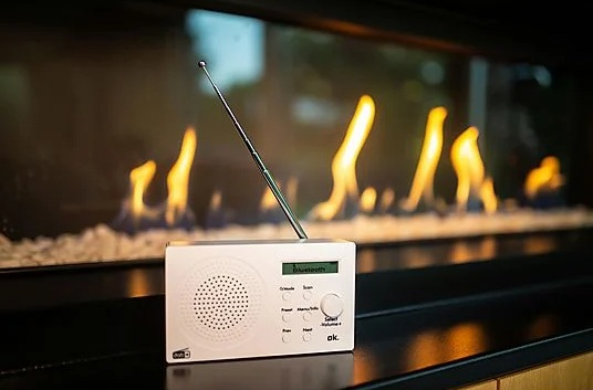 Białe radio z antenką przed kominkiem.