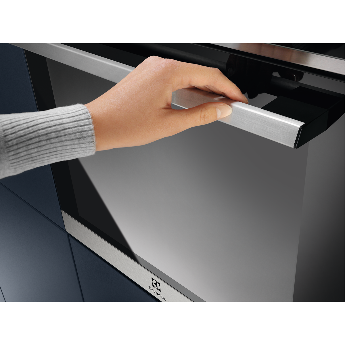 Egy szürke pulóveres kéz ezüst sütőkilincset nyit.