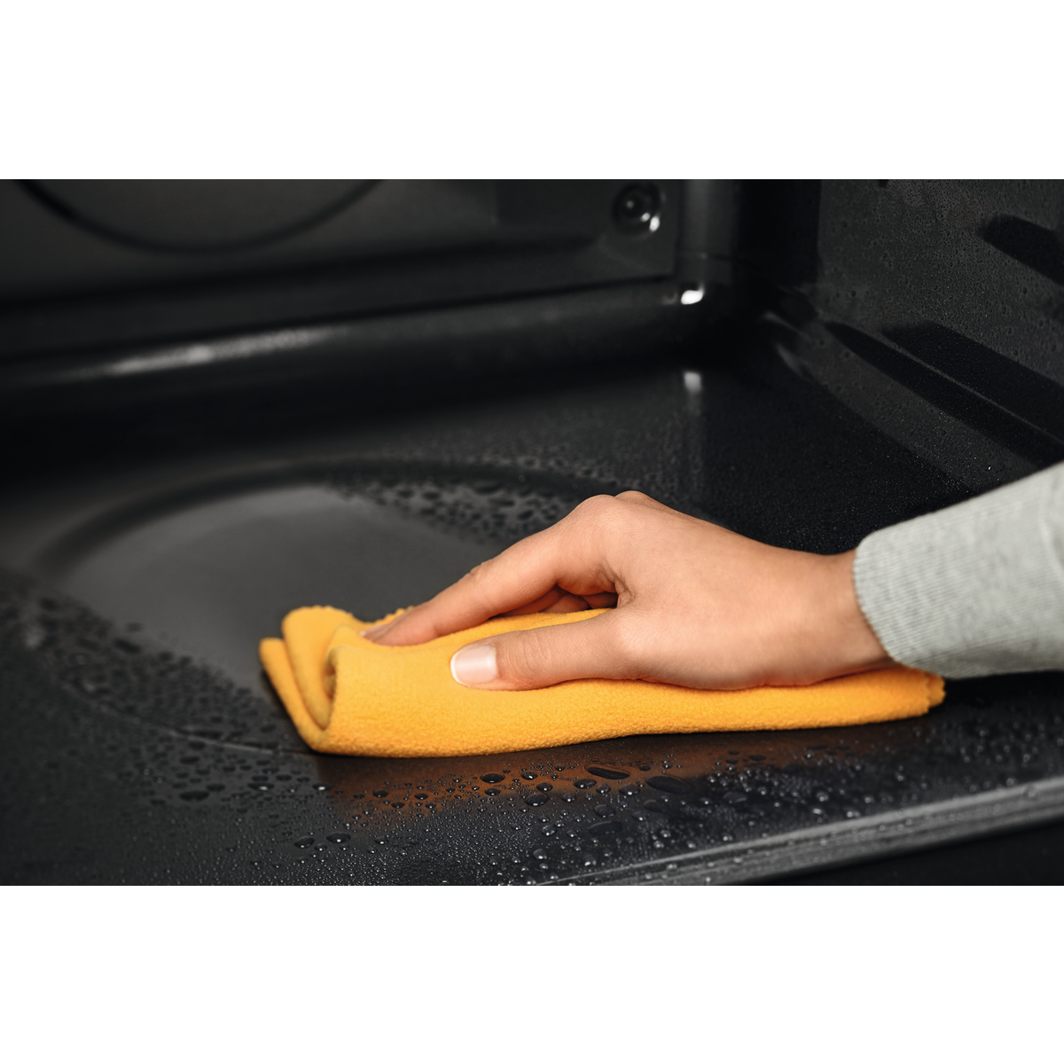 Egy kéz nedves fekete felületet töröl át sárga ruhával.