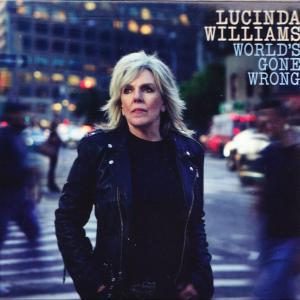 Lucinda Williams steht auf einer belebten Straße bei Nacht, mit Lichtern im Hintergrund.