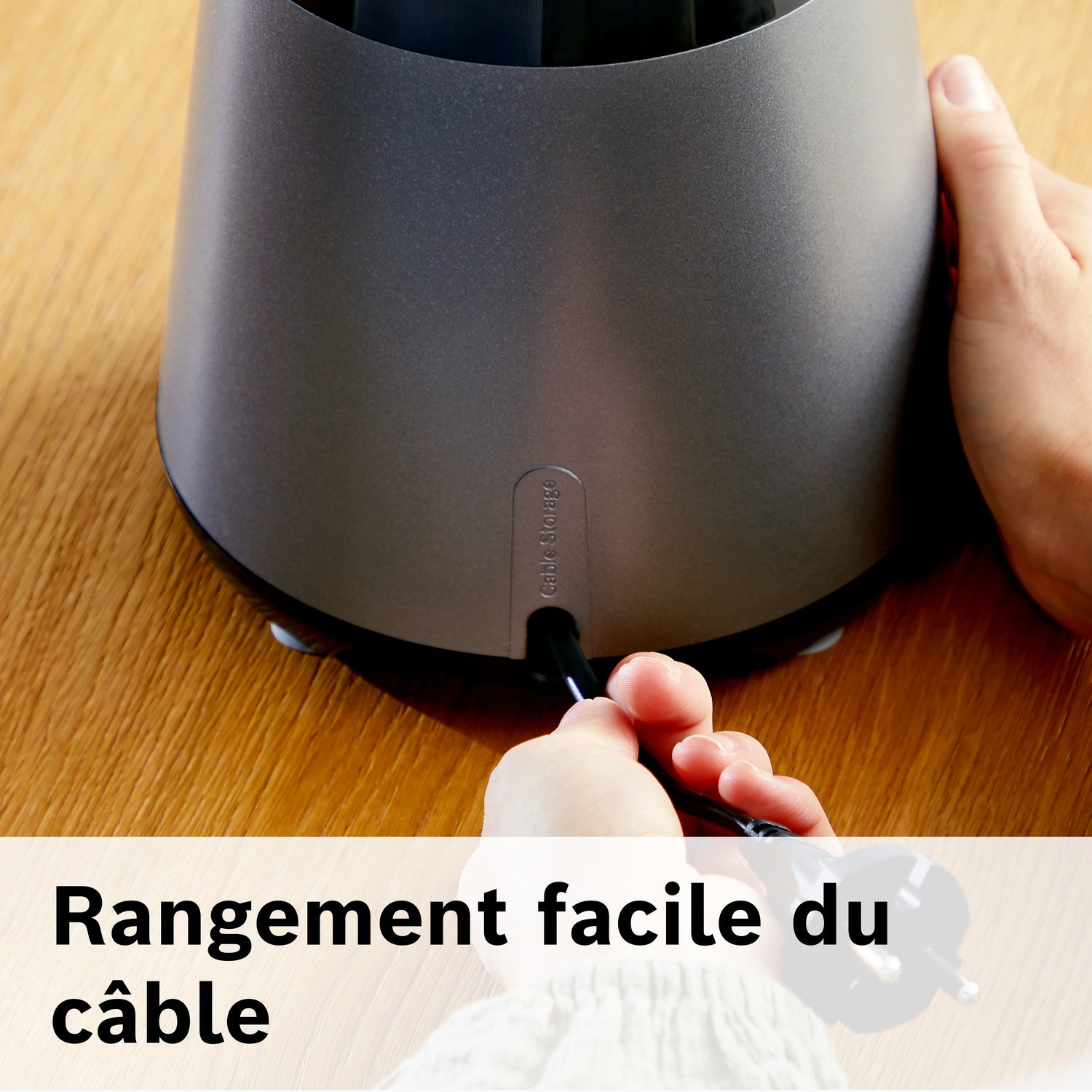 Mains branchant un câble noir dans un appareil gris sur une table bois.