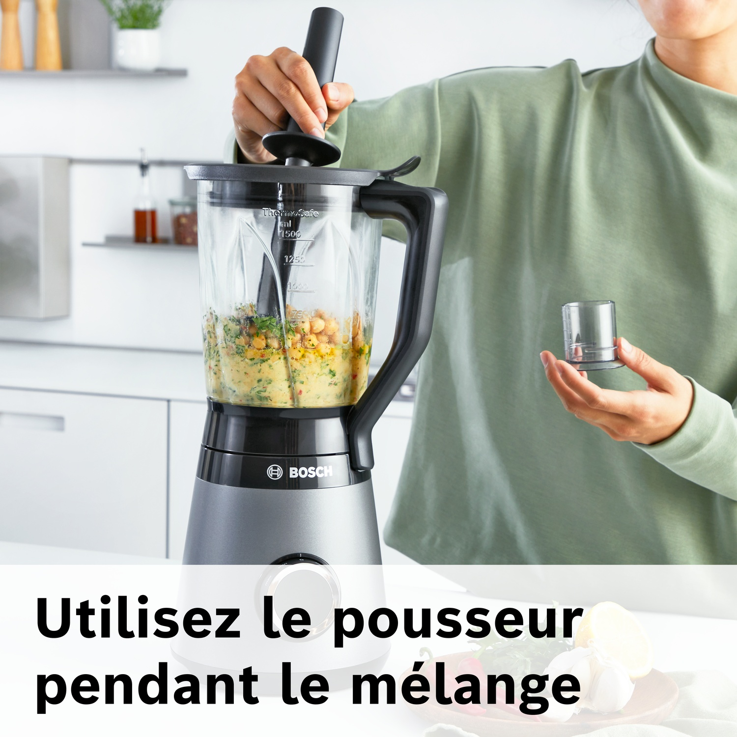 Une personne utilise un mixeur pour préparer un mélange de pois chiches et d'herbes.