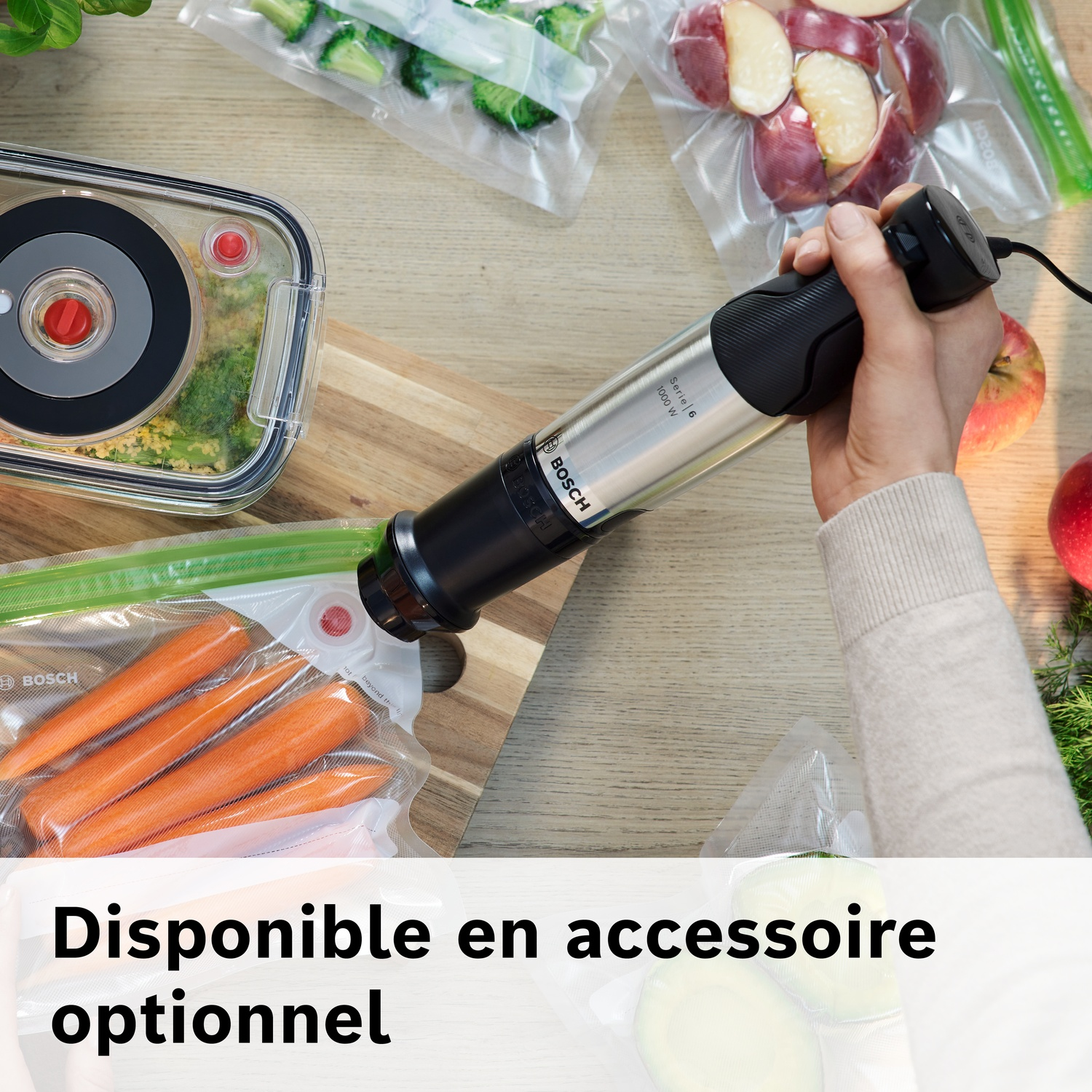 Main tenant un appareil de mise sous vide Bosch sur légumes et fruits scellés.