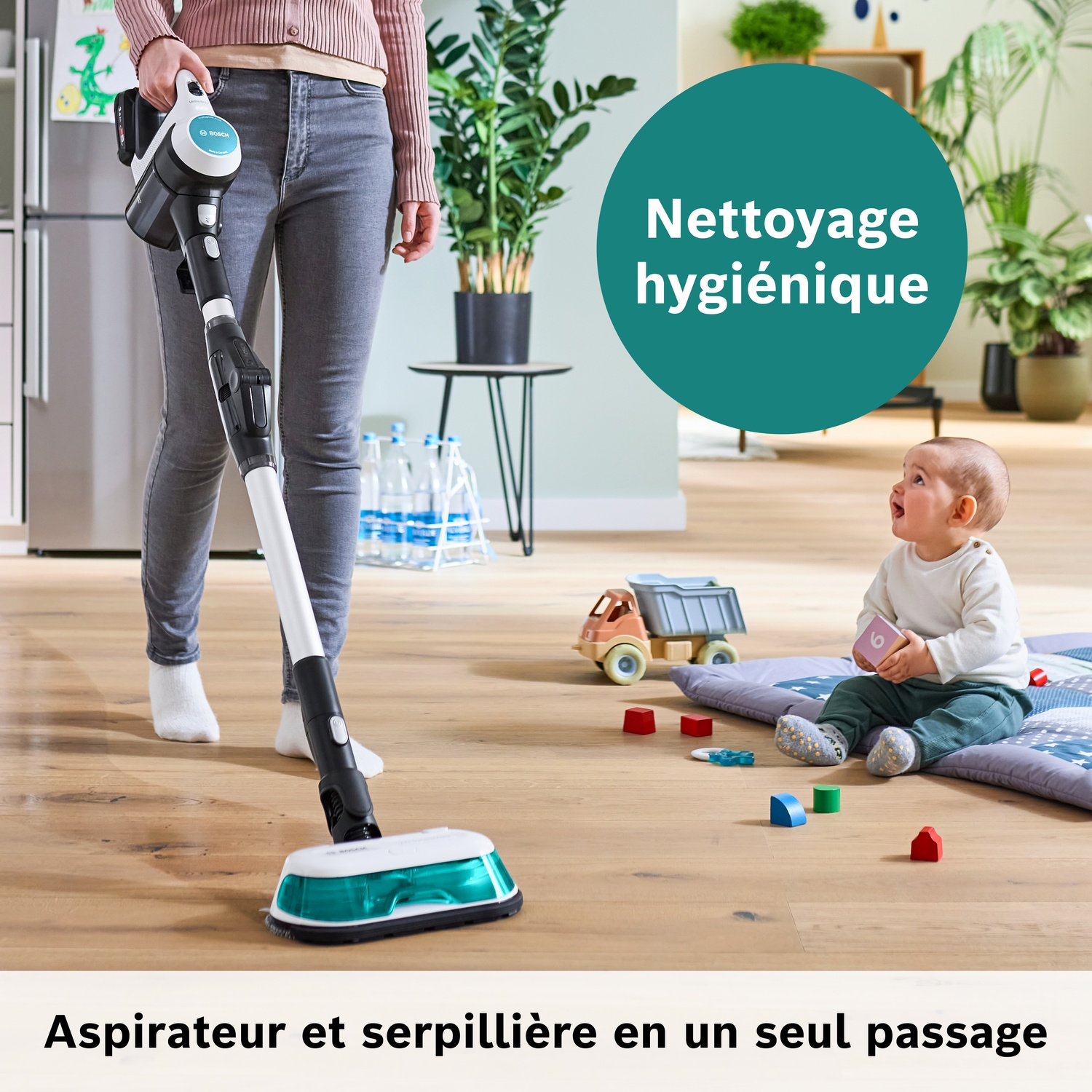 Une personne passe l'aspirateur et lave le sol pendant qu'un bébé est assis sur un tapis de jeu.