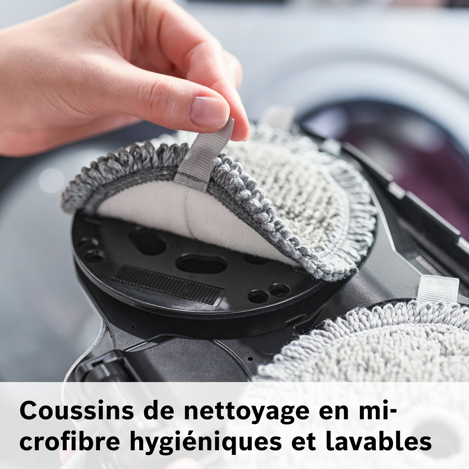 Une main attache un tampon de nettoyage en microfibre gris à un appareil noir.