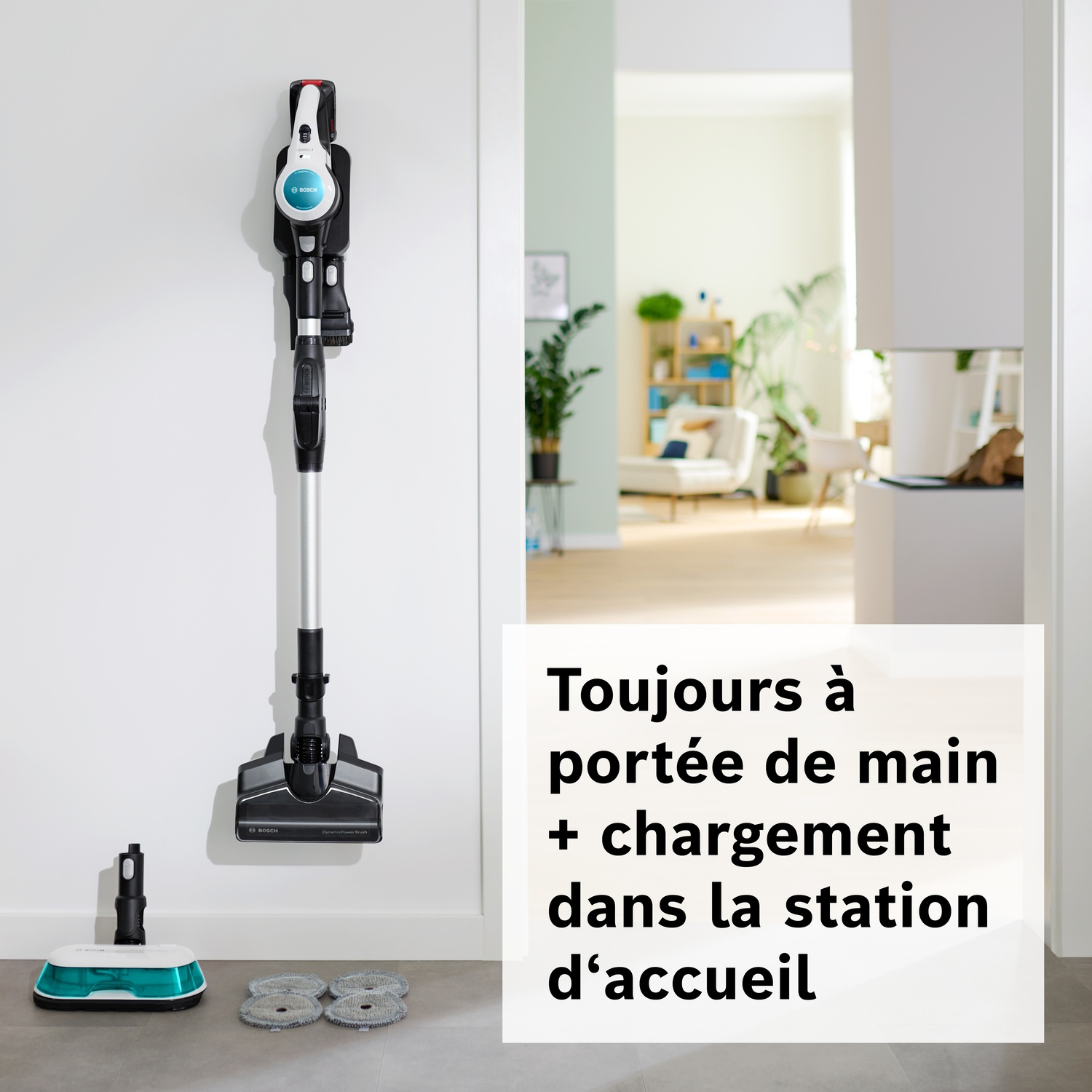 Un aspirateur balai Bosch sans fil est accroché à un support mural. Accessoires au sol.