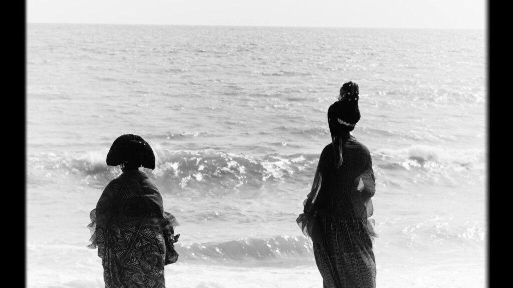 Zwei Personen in Kleidern blicken auf das Meer.