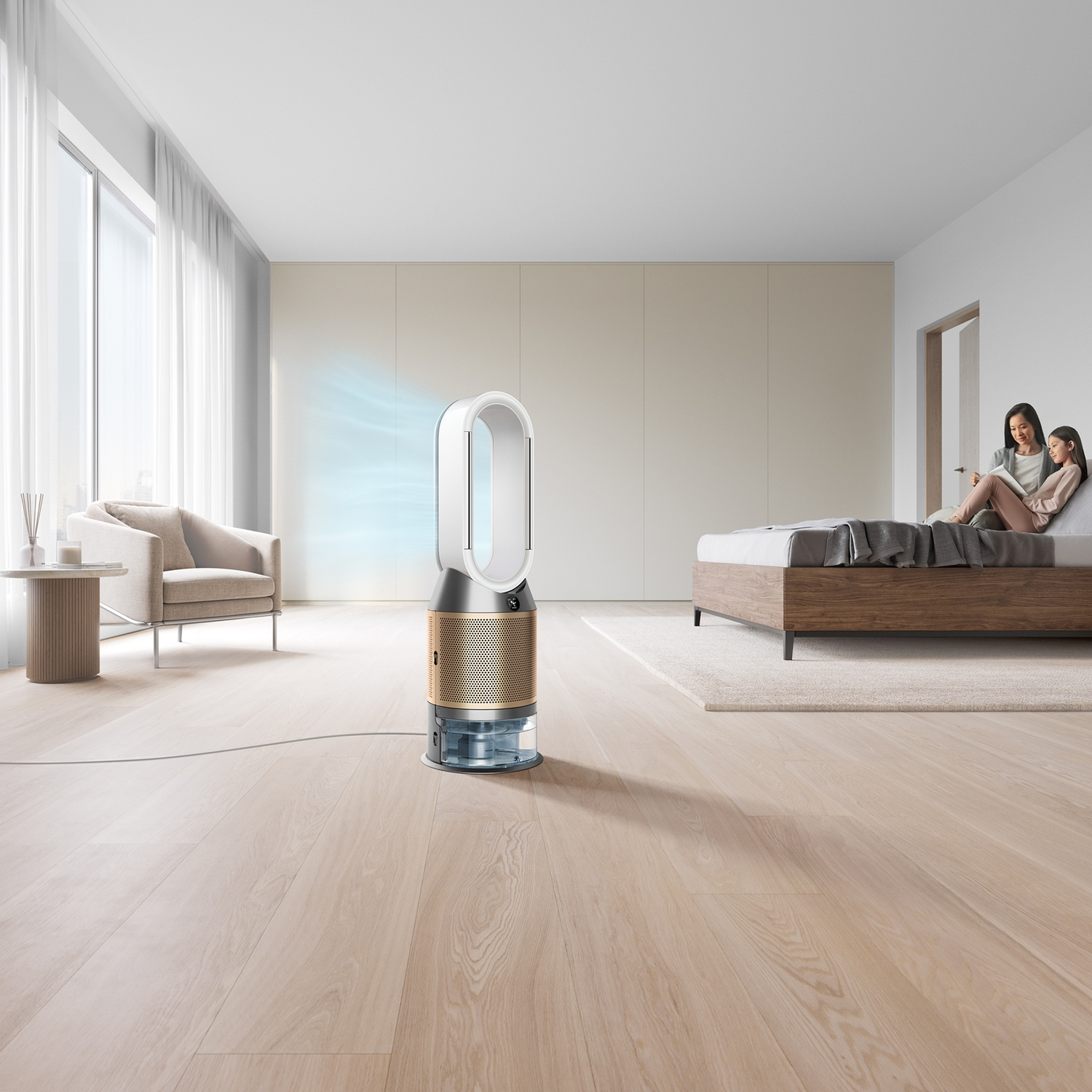 Un purificatore d'aria Dyson si trova su un pavimento in legno in una camera da letto. Due donne sono sedute su un letto.