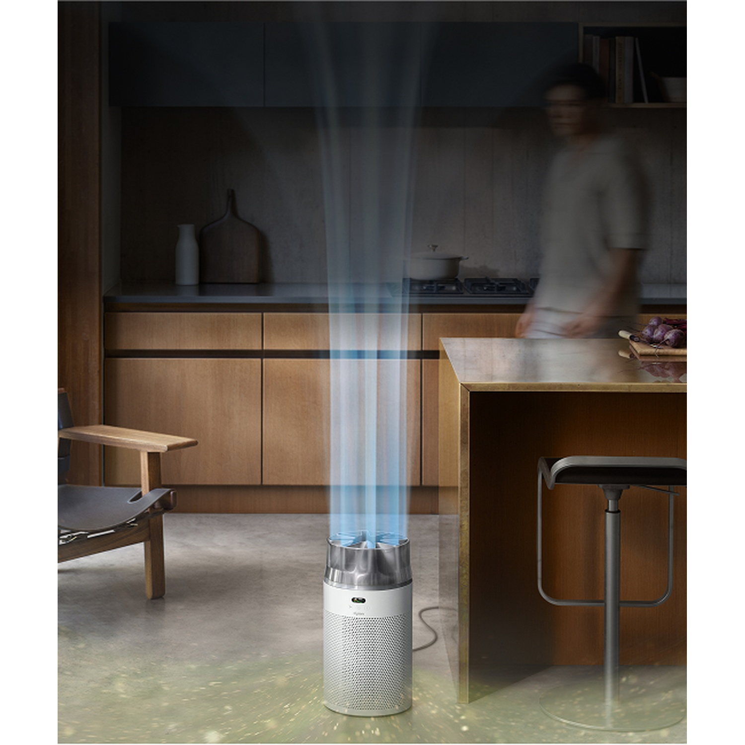 Un purificatore d'aria emette flussi d'aria blu in primo piano. Una persona si trova in una cucina.