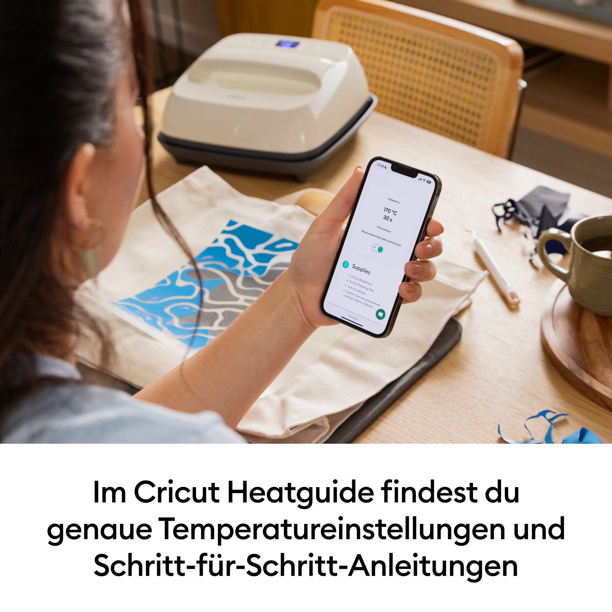 Eine Person hält ein Smartphone mit einer Cricut Heatguide App. Ein Bügeleisen steht daneben.