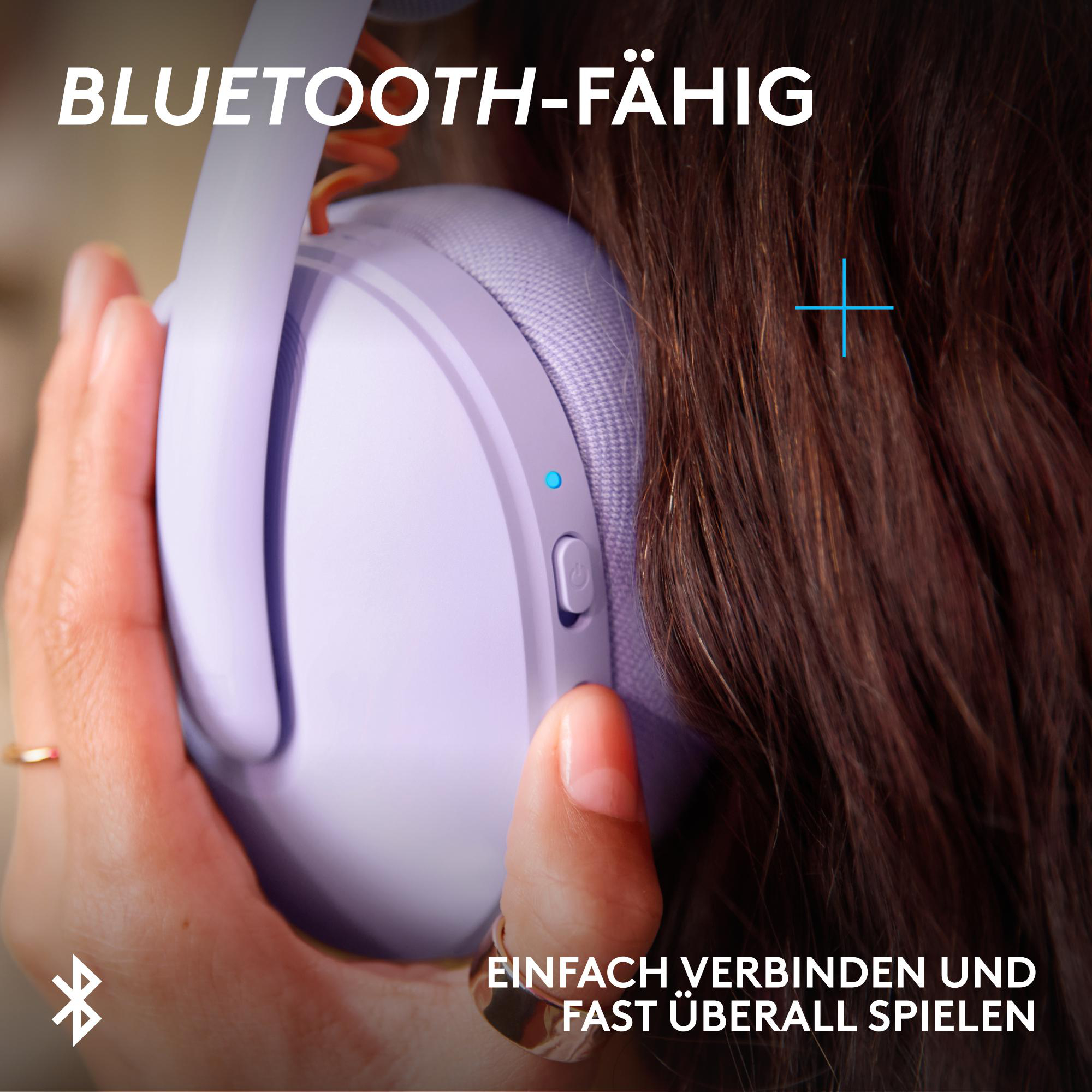 Lila Kopfhörer mit Power-Taste und blauem Licht. Person hält sie.