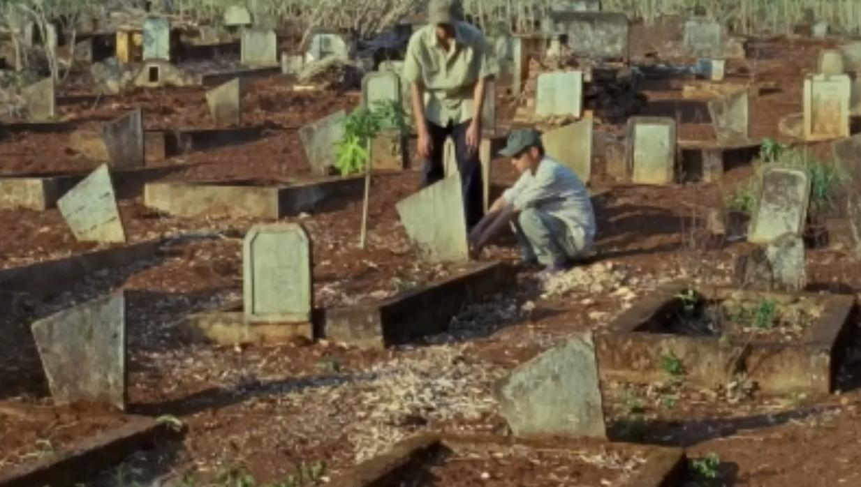 Zwei Männer in einem Friedhof mit vielen Gräbern und Grabsteinen.