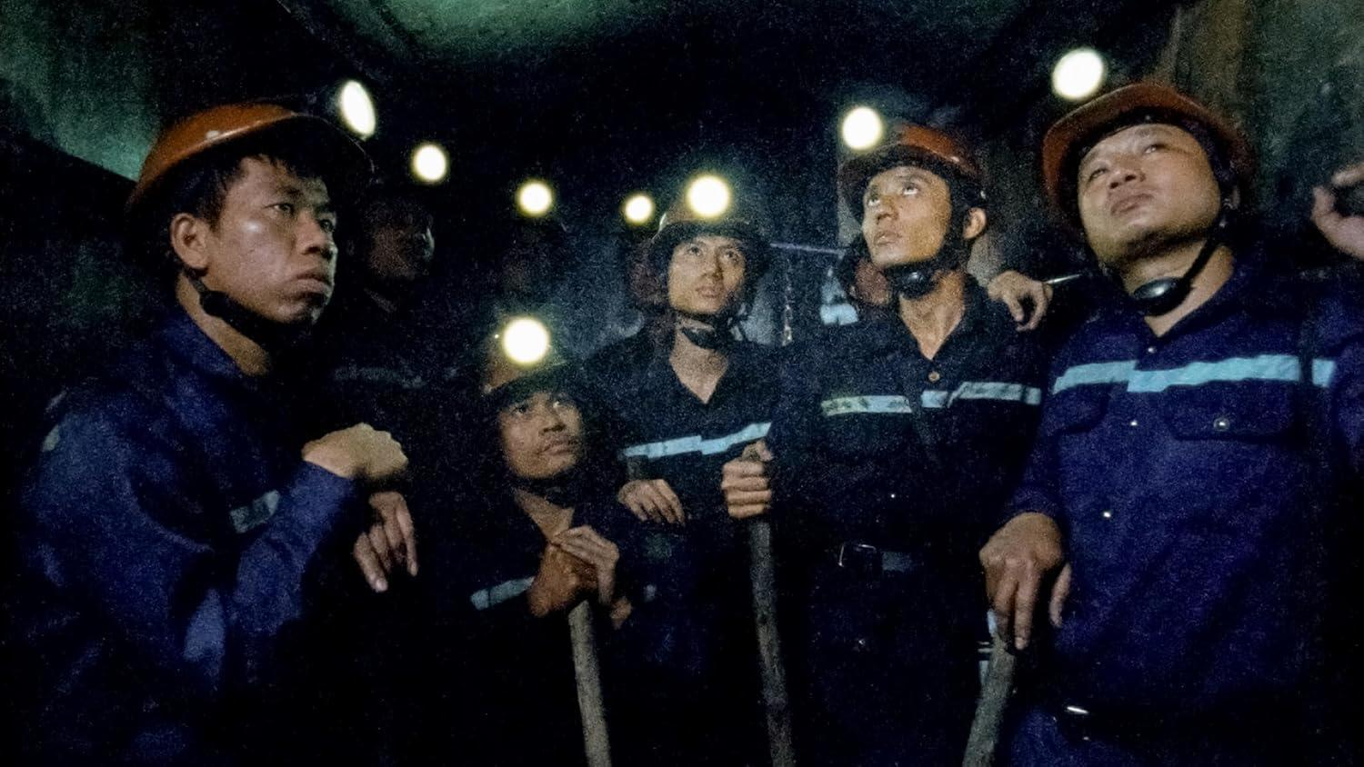 Bergleute mit Helmlampen stehen in einem dunklen Tunnel.