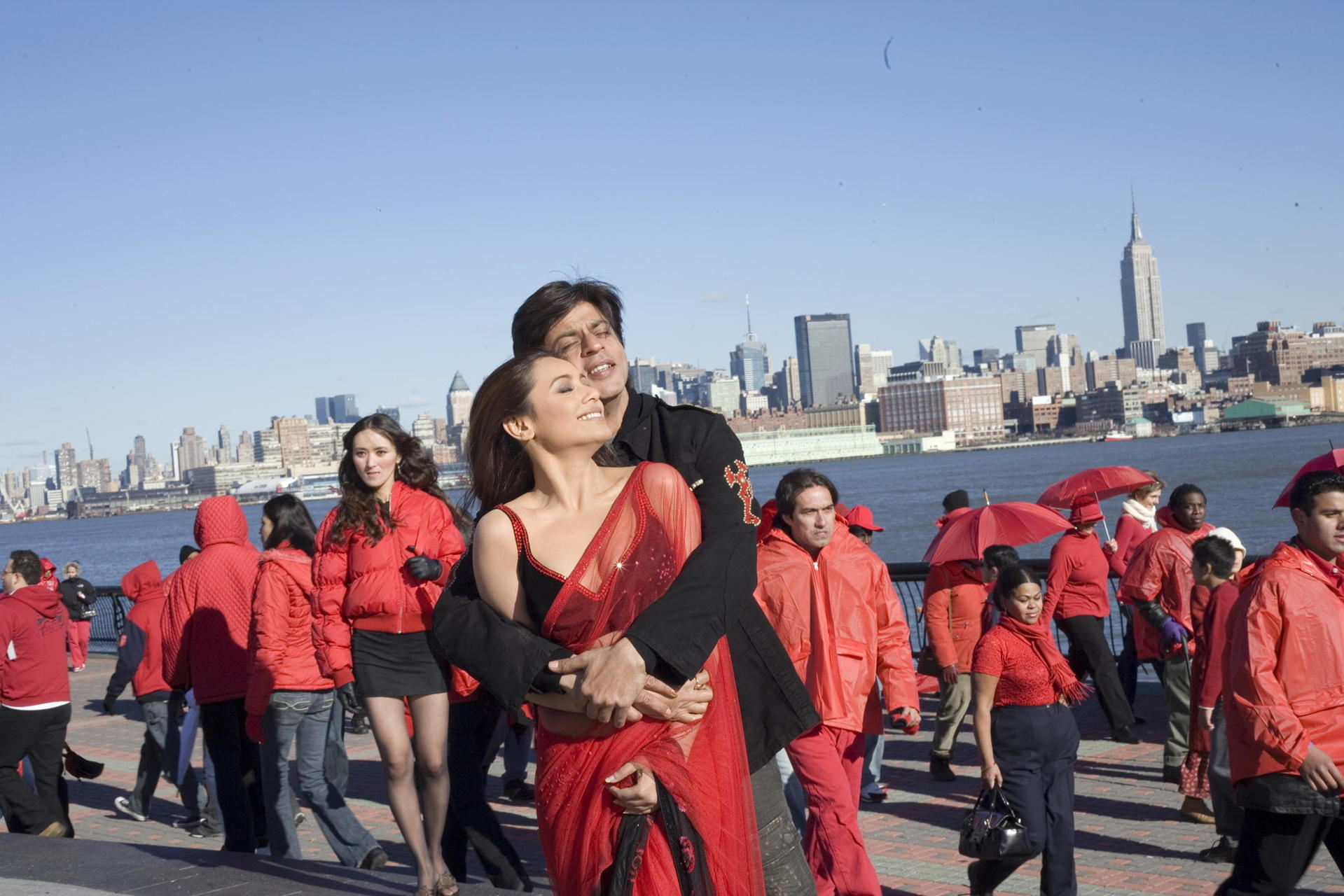 Ein Mann umarmt eine Frau in einem roten Sari vor einer Stadtkulisse mit dem Empire State Building.