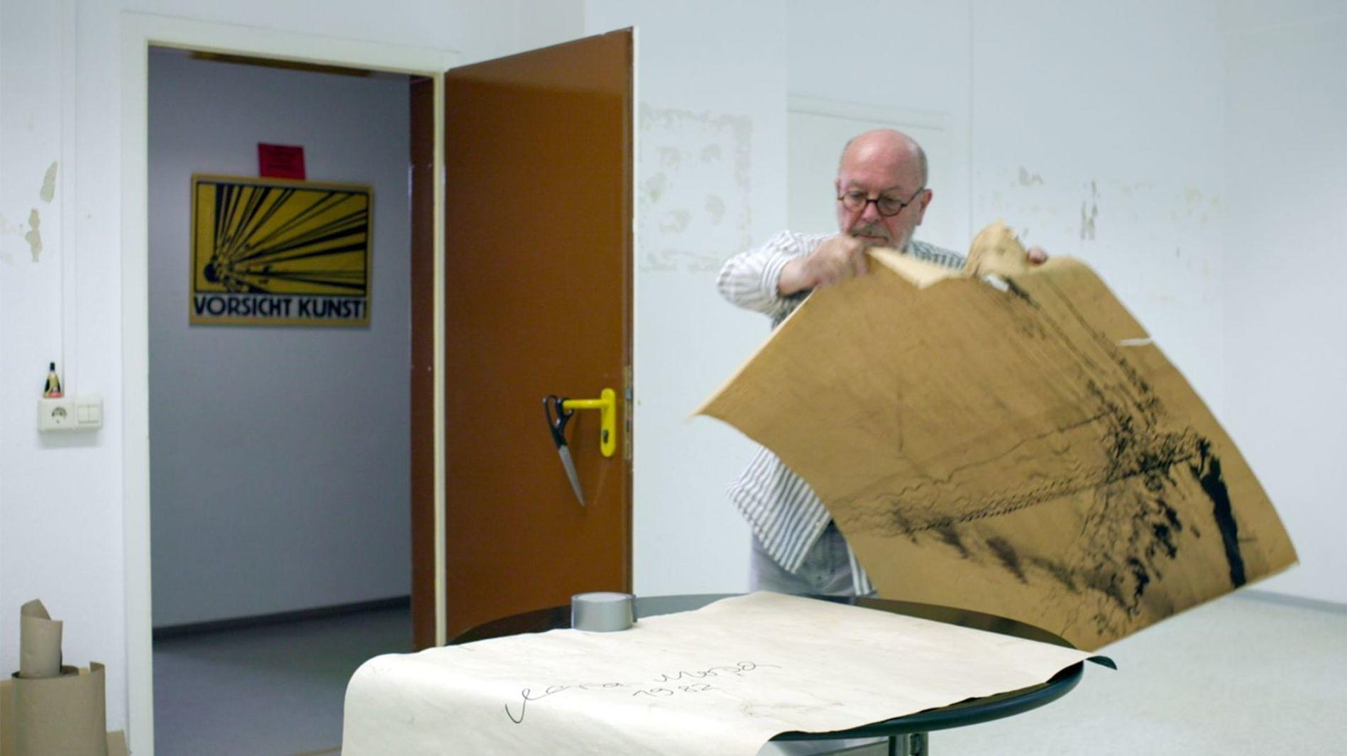 Mann entrollt großes braunes Papier mit schwarzer Zeichnung, drinnen.