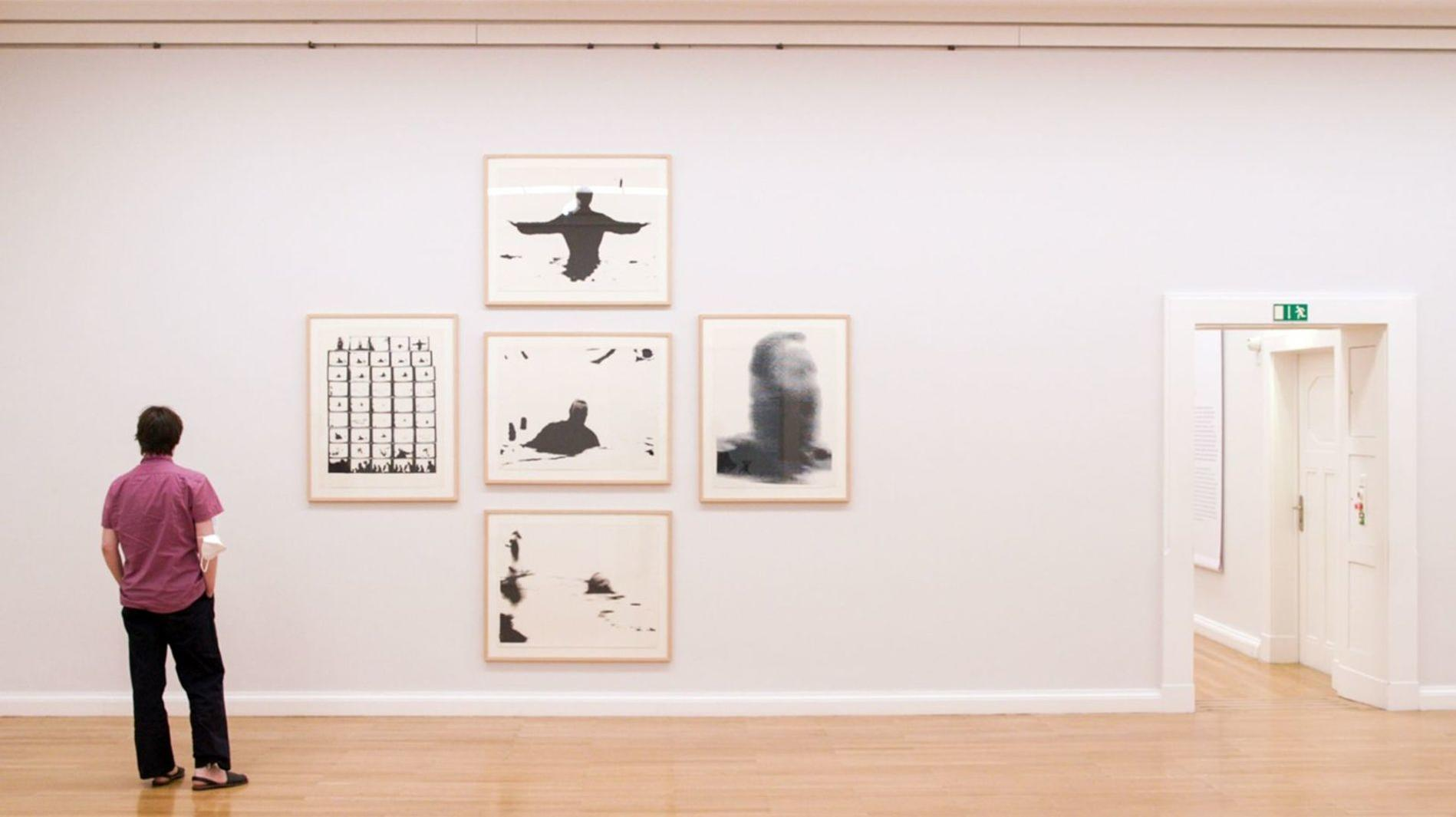 Eine Person in einem lila Hemd betrachtet abstrakte Kunst in einer Galerie mit offener Tür.