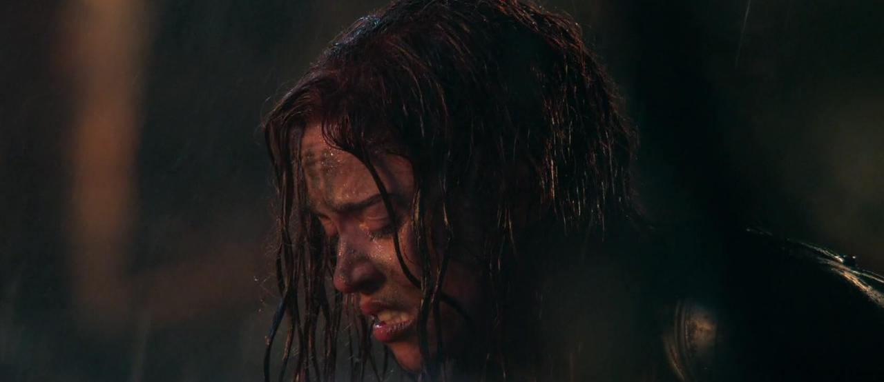 Eine Frau mit durchnässten Haaren und Schmutz im Gesicht weint unter Regen.