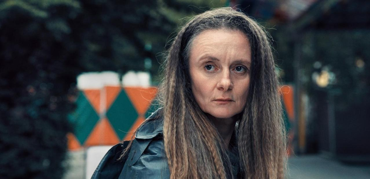 Eine Frau mit langen, braunen Haaren und einem blauen Mantel steht im Freien.