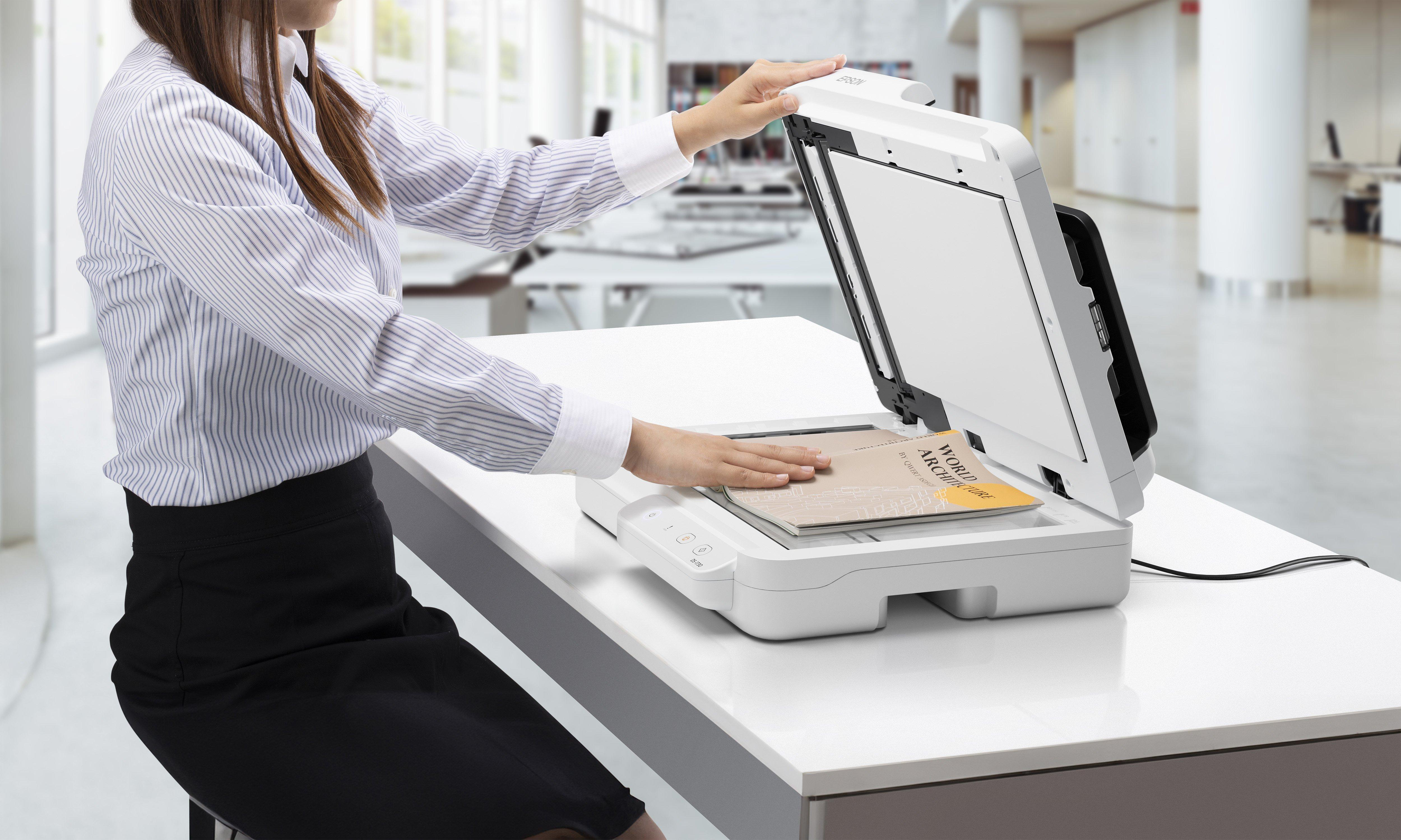 Eine Frau legt ein Buch in einen weißen Scanner im Büro.