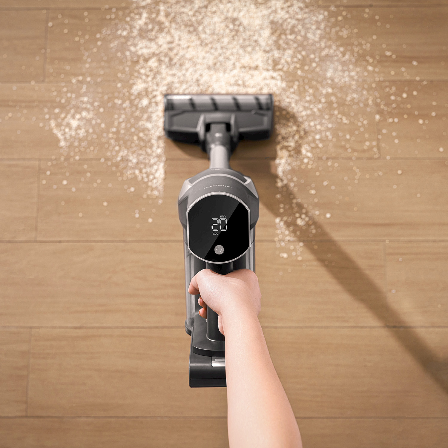 Una mano tiene un aspirapolvere grigio che aspira polvere su un pavimento di legno.