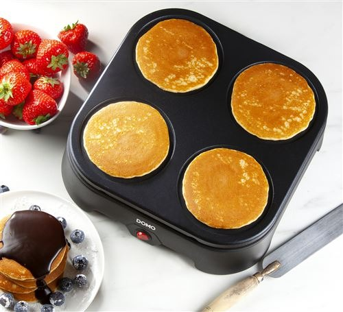 Electric pancake maker with four golden-brown pancakes and strawberries nearby.