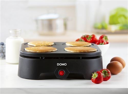 A black pancake maker with four pancakes, eggs, and strawberries on the side.