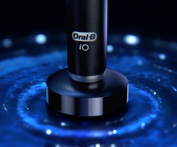 Czarna szczoteczka Oral-B iO na ładowarce z niebieskim tłem.