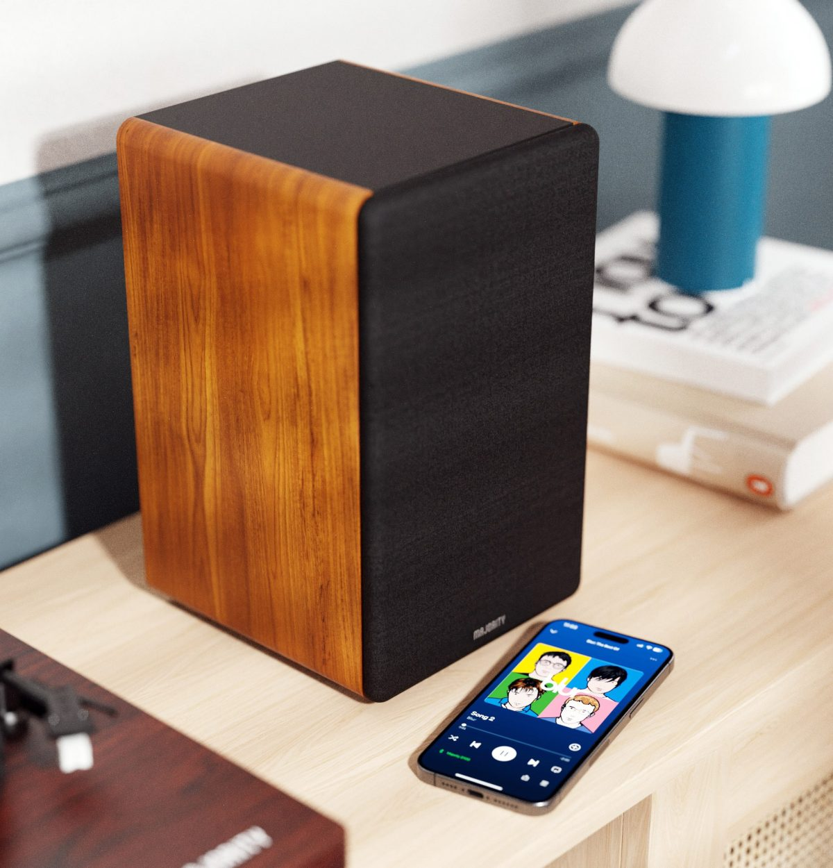Ein Lautsprecher mit Holzoptik und schwarzem Stoff neben einem Smartphone mit Musik-App.
