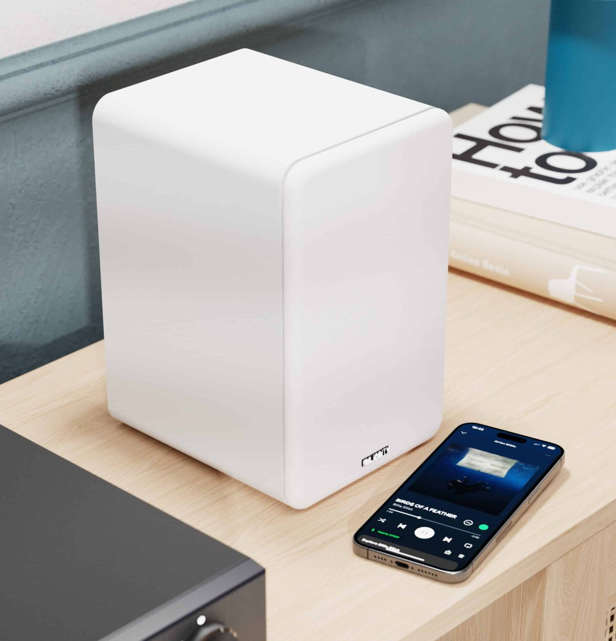 Ein weißer Lautsprecher steht neben einem Smartphone mit Musik-App.